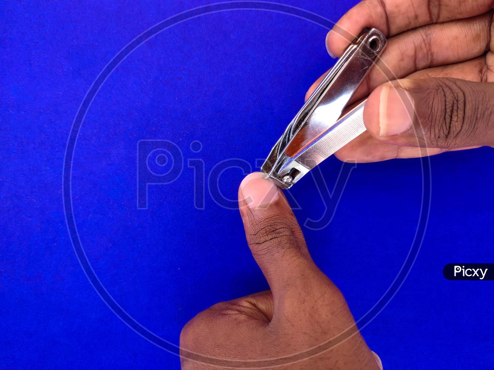 Close Up Of Man Cutting His Thumb Finger Nail. Isolated On Blue Background.