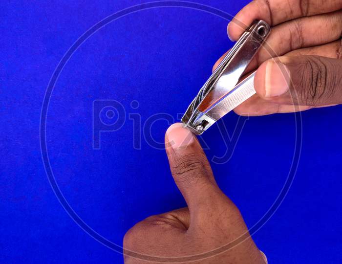Close Up Of Man Cutting His Thumb Finger Nail. Isolated On Blue Background.