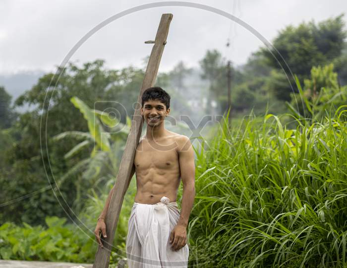 Happy Indian Farmer Standing With Wooden Plough In Rice Field
