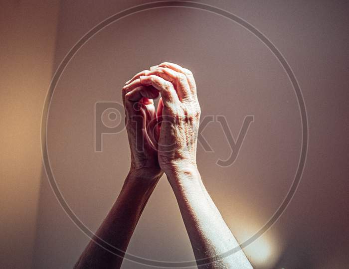 Old Woman Hands Raised In Religious Position Asking For Something In Pink Tones With Bright Lights