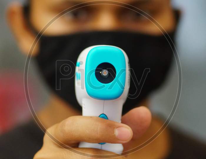 A security personnel using Infrared Thermometer using Laser Radiation to find out the Human Body temperature as fever is one of the symptoms of COVID19 Corona Virus