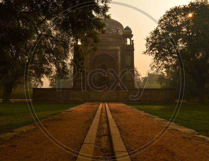 Bunch Of Trees And Mesmerizing View Of Humayun Tomb Memorial From The Side Of The Lawn At Winter Foggy Morning.