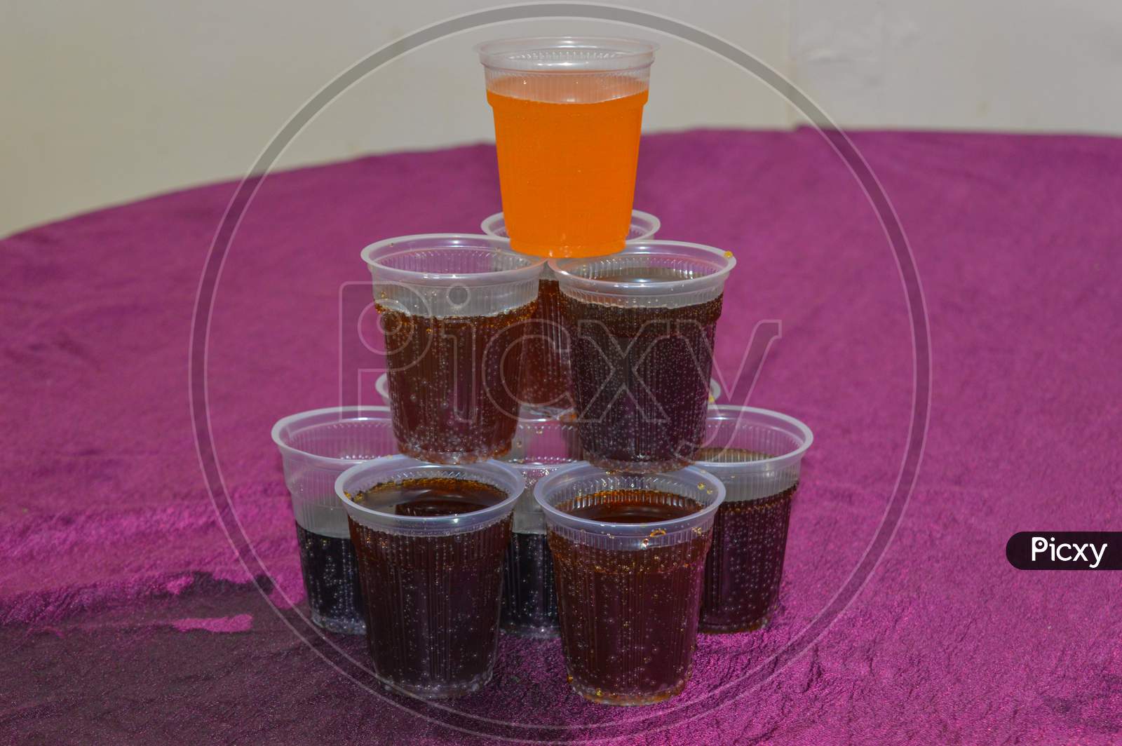 A Pyramid Of Cold Drink In Plastic Glasses Isolated On Purple Table.