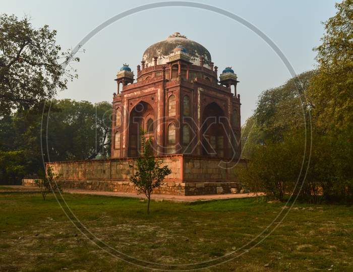 Bunch Of Trees And Mesmerizing View Of Humayun Tomb Memorial From The Side Of The Lawn At Winter Foggy Morning.