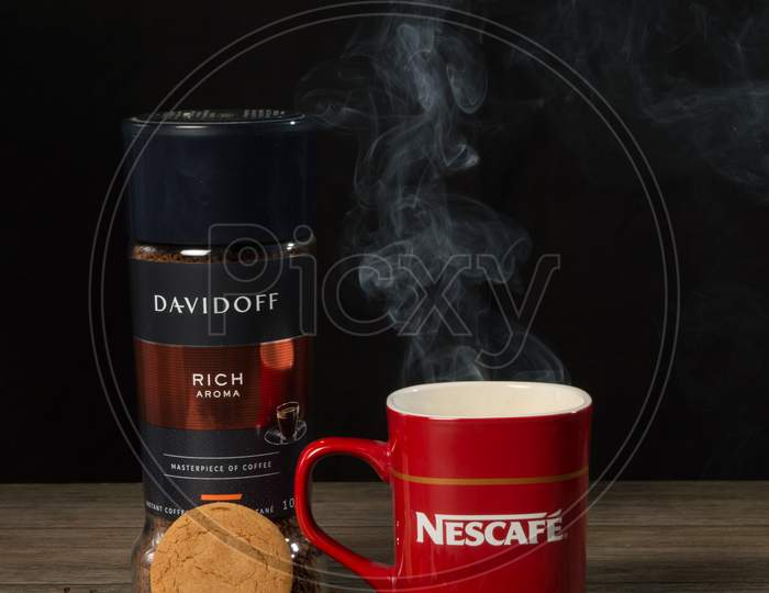 Smoky Coffee In Red Nescafe Mug With Raw Coffee Beans, Cookies, David Off Coffee On A Table And Black Background.