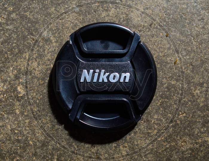 A Lens Cap Of Nikon Camera Lens Isolated On Texture Cemented Floor.