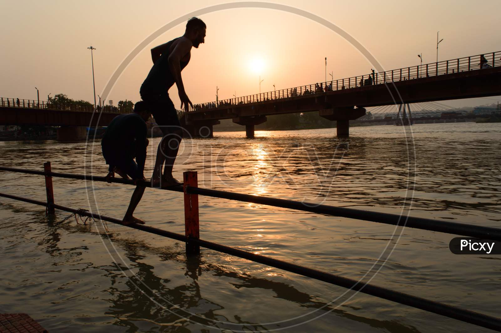 Two Boys Going To Jump Into Ganga River For Relief Of Heat In Summer At Sunrise At Haridwar Bridge Temple Sky.