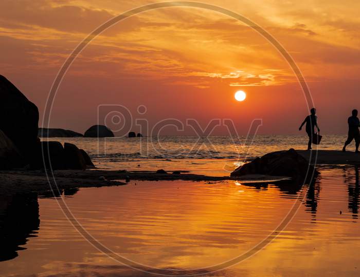 Sunrise captured at a low angle with reflections on the water and men walking across