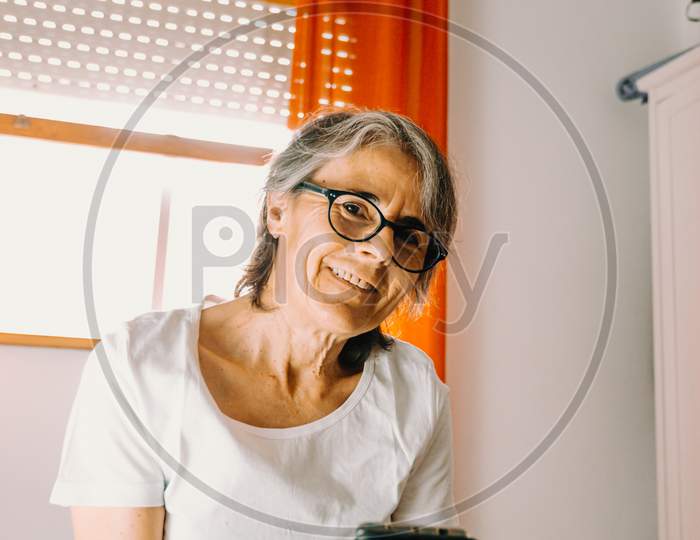 Close Up Of An Old Female Smiling To Camera While Grabbing His Phone In His Bedroom