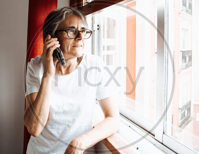 Old Woman Making A Call On The Mobile Phone While Looking Through The Window