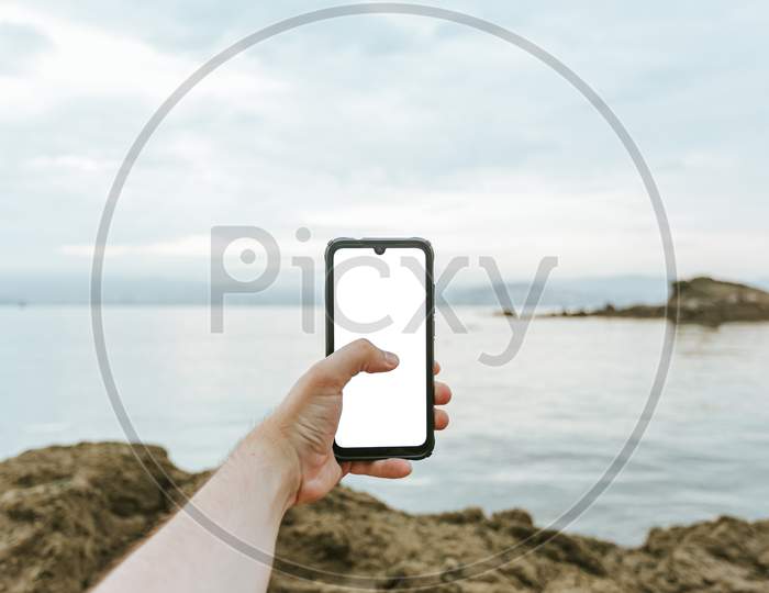 Young Male Hand Grabbing A Phone With Copy Space With The Sea As The Background