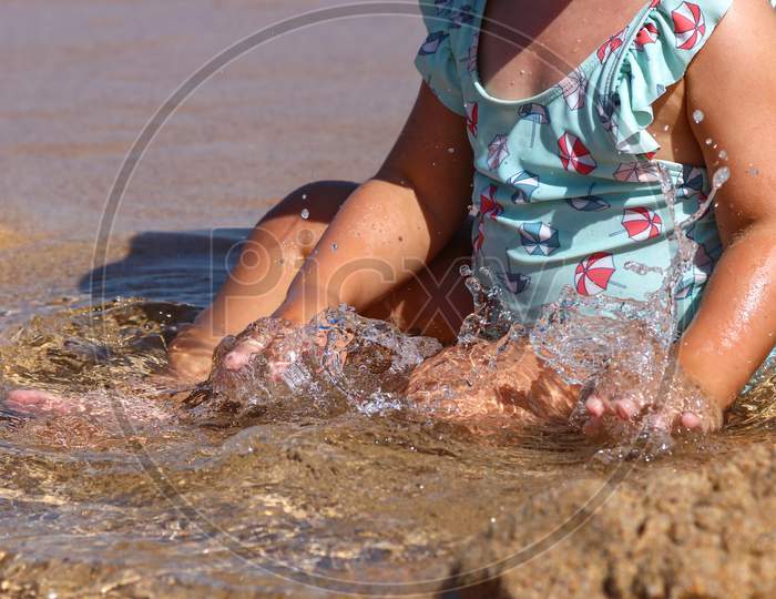 Small child in colorful swimsuit with hands in water