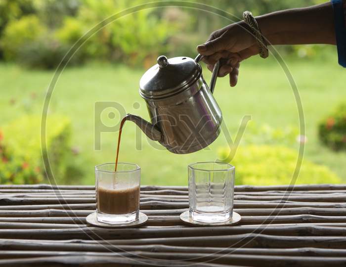 Morning Tea Serving In A Glass On A Bamboo Table From A Steel Kettle In A Beautiful Green Garden