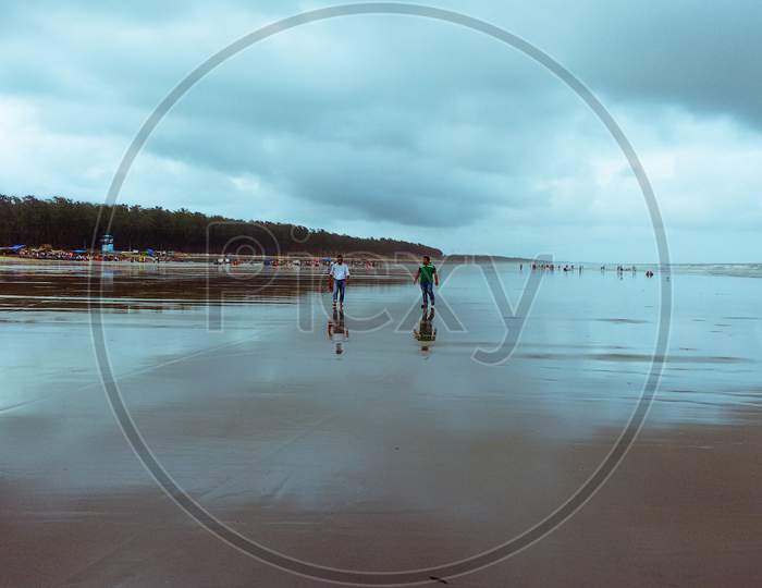 Two friends walking in the sea beach in cloudy weather