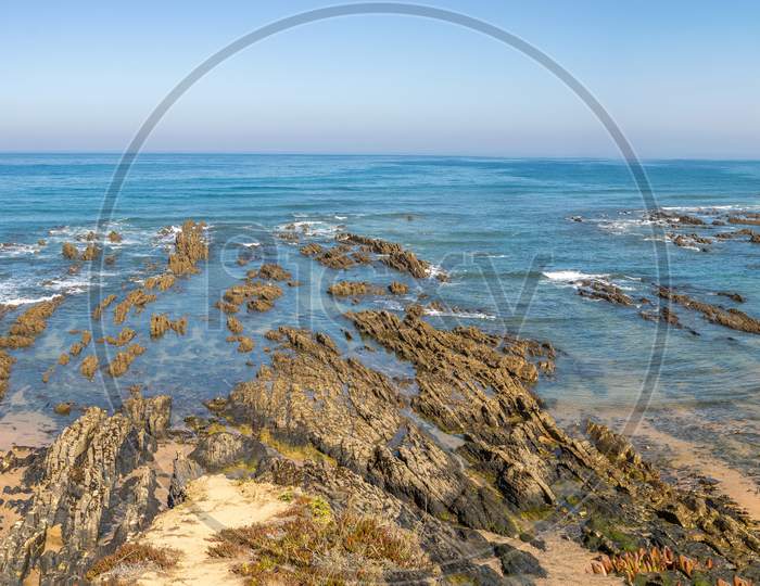 Wide panoramic view of beach in Costa Vicentina, Alentejo. Rocky beach, Atlantic ocean, cliff side with rocks. Amazing blue water and clear blue sky.