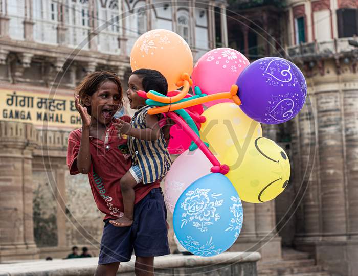 A little girl selling balloon on varanasi ghat and taking care her younger brother like a mother