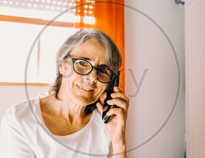 Close Up Of An Old Female Taking A Call On The Phone While Smiling In His Bedroom