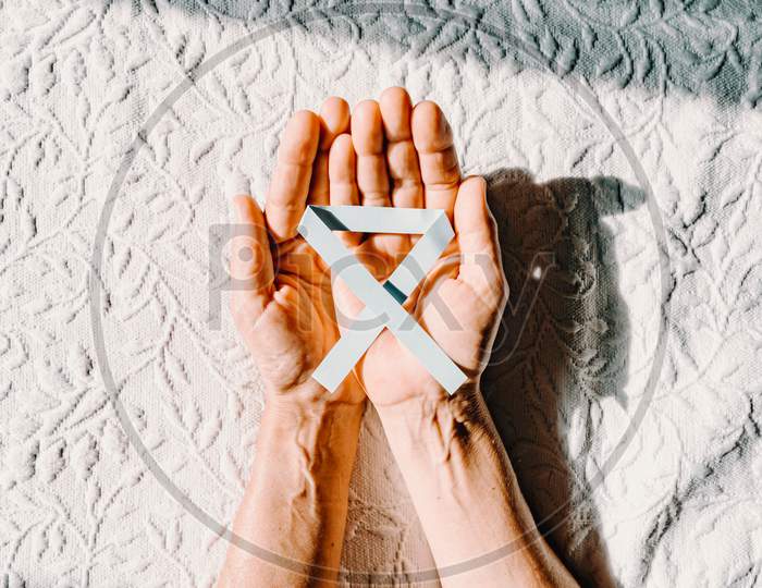 Vertical Image Of Two Old Hands Grabbing A Blue Ribbon For The International Diabetes Day
