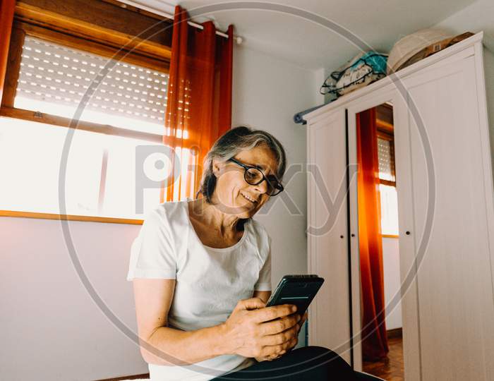 Old Woman Checking His Phone In His Bedroom