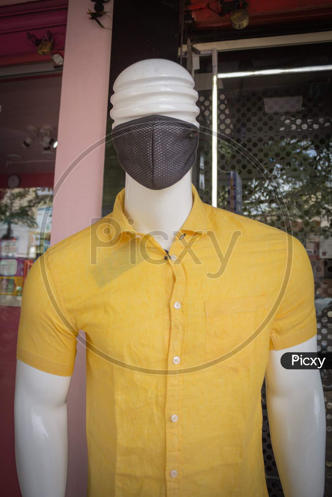 A Pretty picture of a Handsome Mannequin dressed in Yellow Cotton Shirt and a Black Face protection Mask at a street side store in Mysuru cityscape of Karnataka state in India.