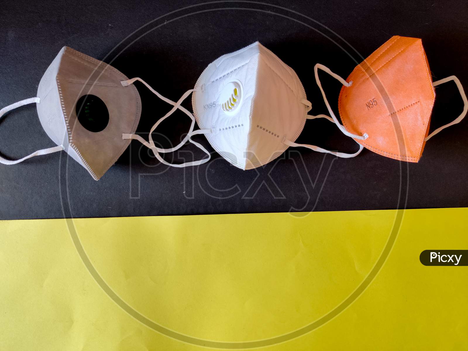 Three Kn-95 Face Masks In White,Grey And Orange Color. Isolated On Black And Yellow Background. Protection From Coronavirus Or Covid-19. Copy Space.Top View
