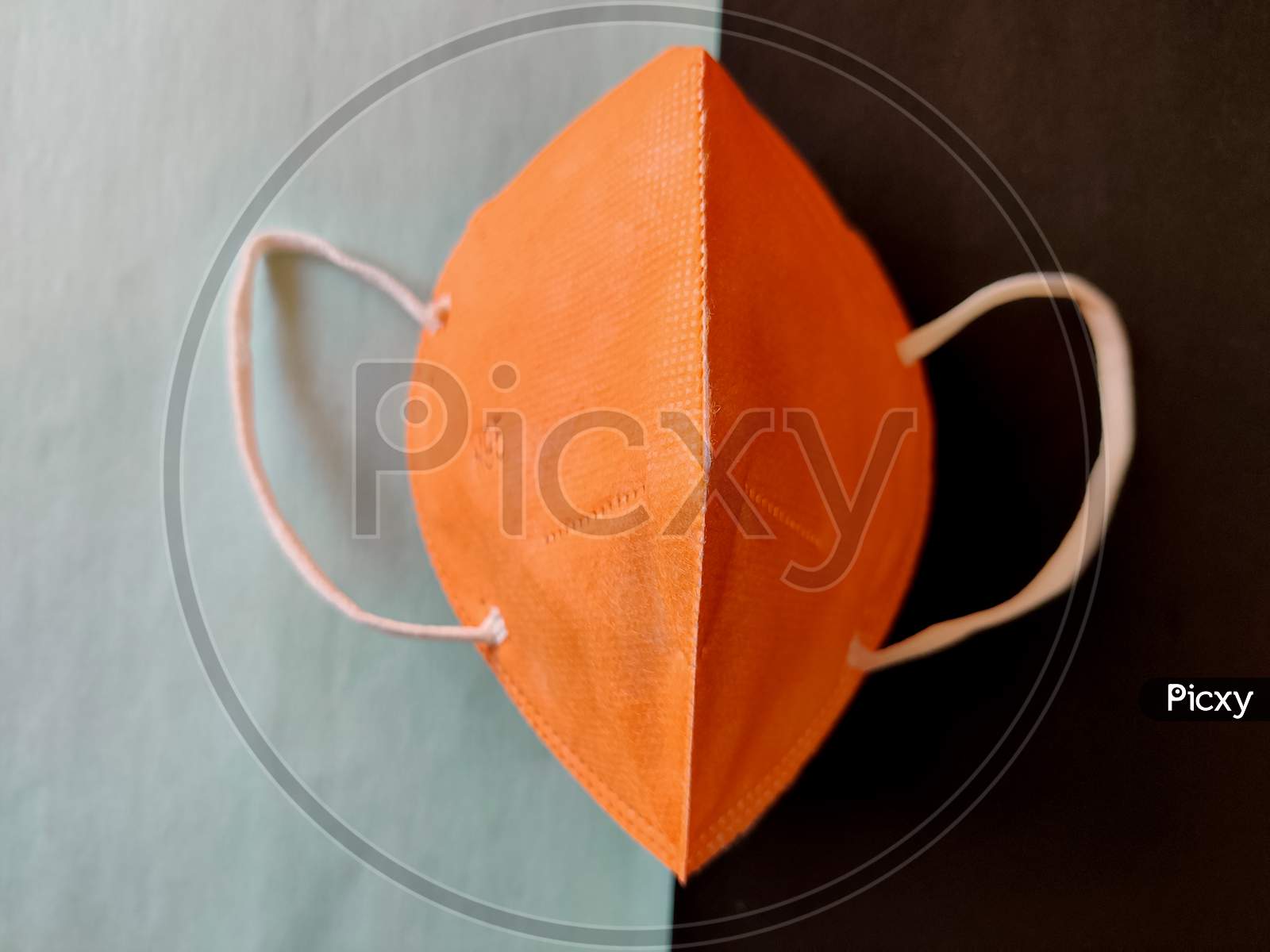 One Orange Color Kn-95 Face Mask Without Filter Cap Isolated On Black And Green Background. Protection From Coronavirus Or Covid-19. Wear A Mask. Coronavirus Pandemic. Top View