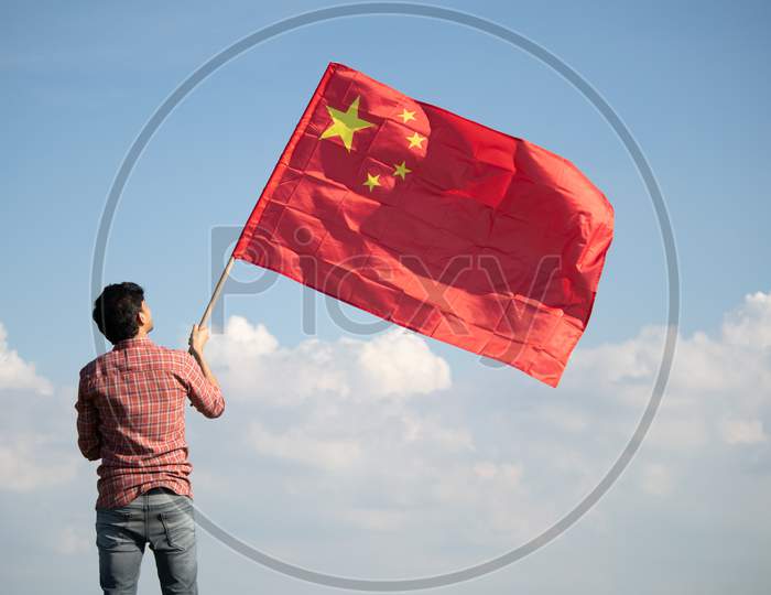 Young Man Proudly Holding Waving Chinese Flag On Top Of Mountain Peak - Concept Showing Celebration Of Chinese Republic Or National Day