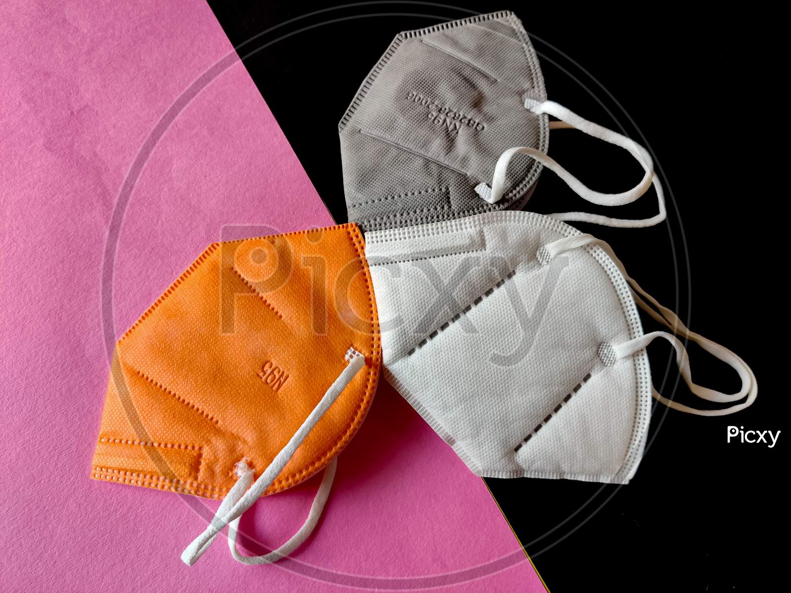 Three Kn-95 Face Masks In White,Grey And Orange Color. Isolated On Black And Pink Background. Protection From Coronavirus Or Covid-19. Top View