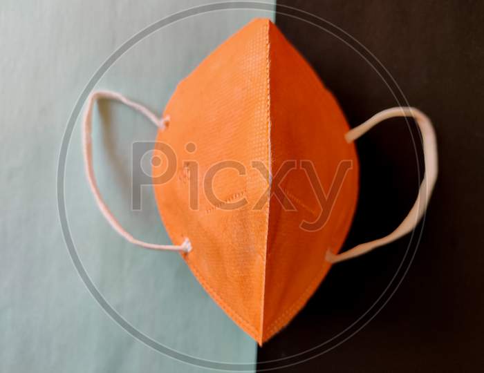 One Orange Color Kn-95 Face Mask Without Filter Cap Isolated On Black And Green Background. Protection From Coronavirus Or Covid-19. Wear A Mask. Coronavirus Pandemic. Top View