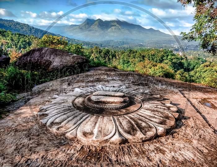 Stone Sculpture Of Feet Near A Jain Temple In Wayanad With Foggy Chembra Peak Hills As Background. Ancient Architecture.