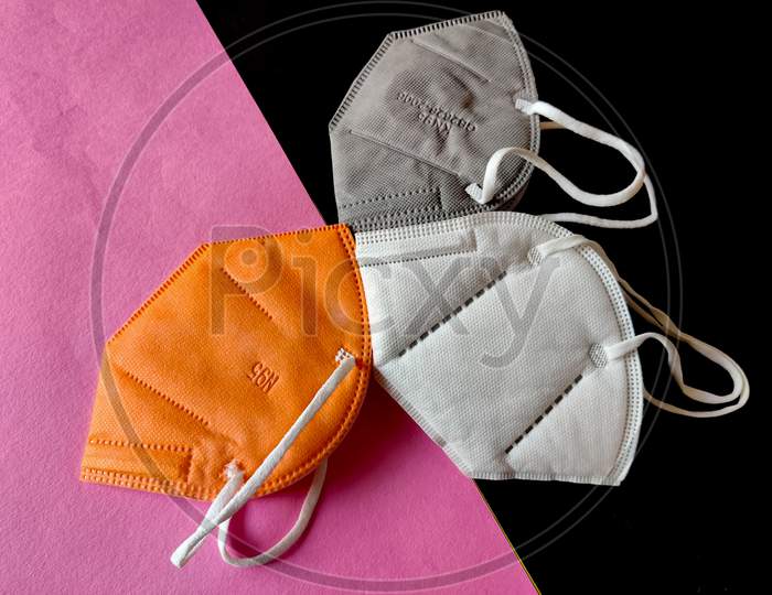 Three Kn-95 Face Masks In White,Grey And Orange Color. Isolated On Black And Pink Background. Protection From Coronavirus Or Covid-19. Top View