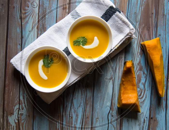 Pumpkin cream soup in two small bowls with vegetable ingredients
