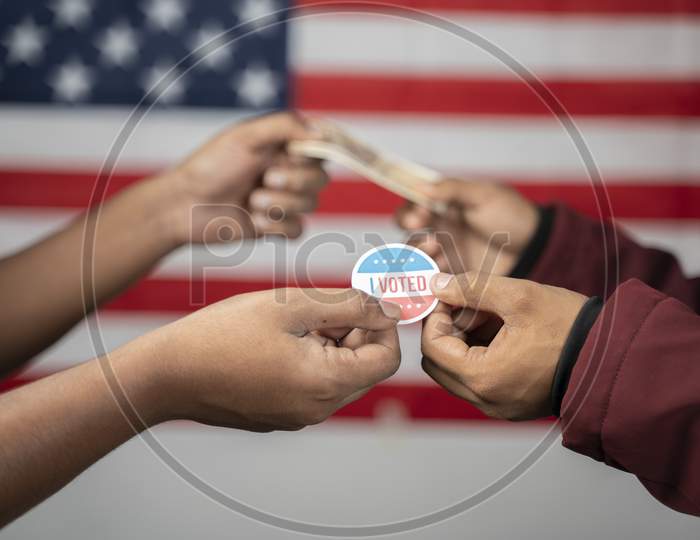 Concept Of Buying Votes In Us Election Showing By Exchanging I Voted Sticker With Money On Us Flag As Background.