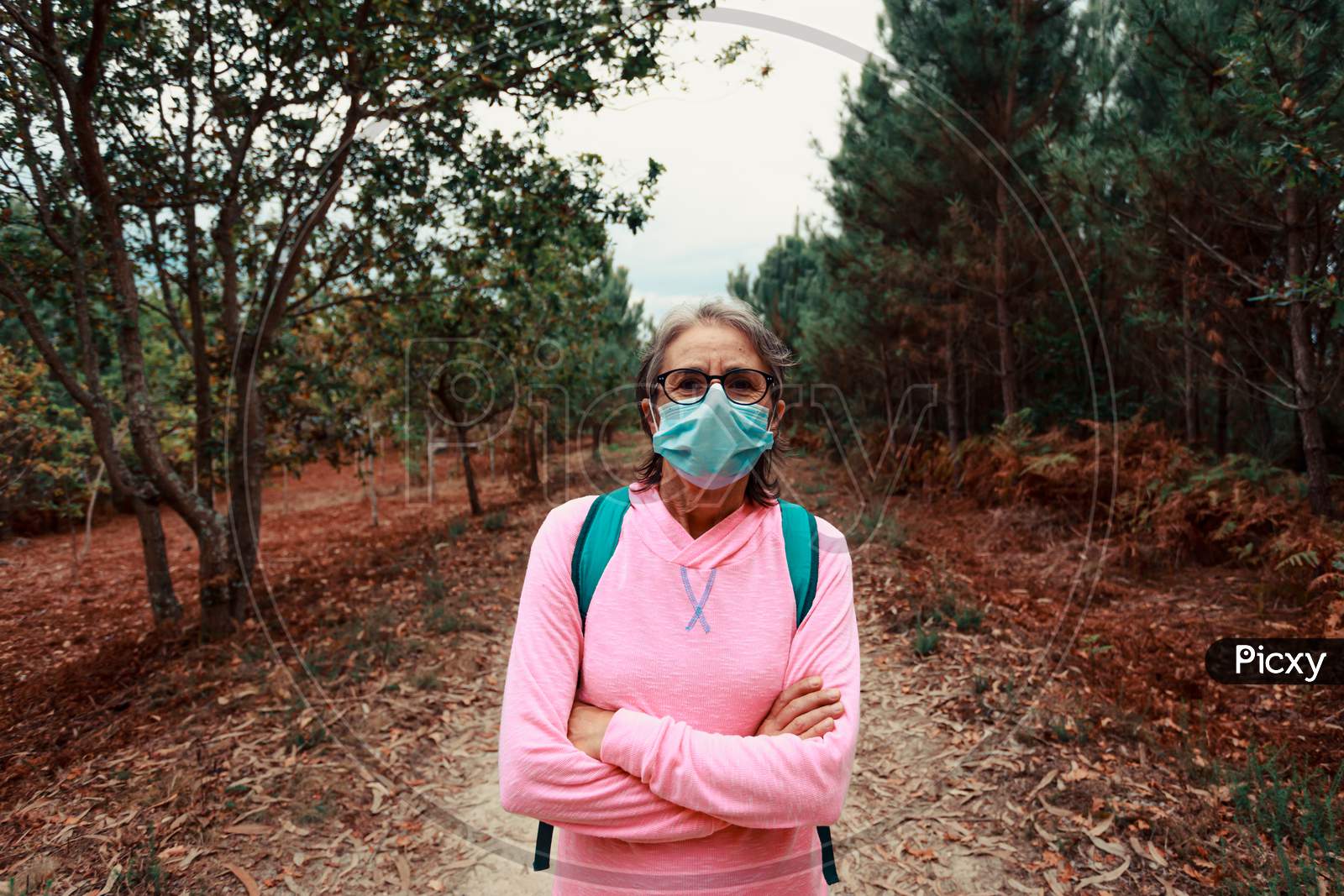 Frontal Portrait Of An Old Woman Wearing A Mask And Sport Clothes In The Forest During A Trekking Day