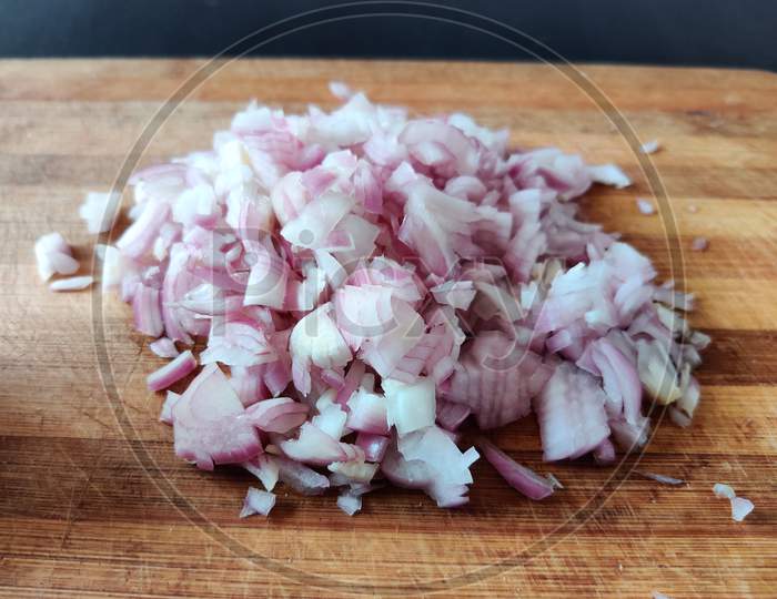 Close Up Of Uncooked Onion Chopped Into Small Cubes Or Pieces. Isolated On Wooden Board.