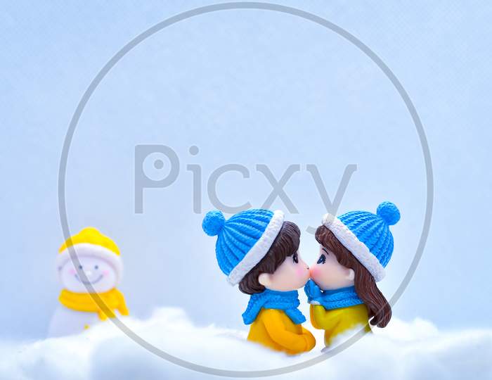 Tourism And Travel Concept: Miniature People Kissing Each Other In Winter Snow With Little Snowman In The Background