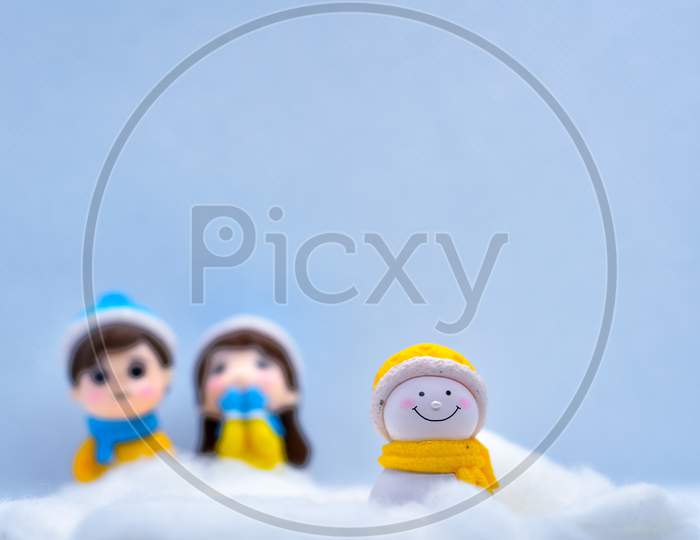 Tourism And Travel Concept: Miniature Little Snowman In Winter Snow With Couple In The Background