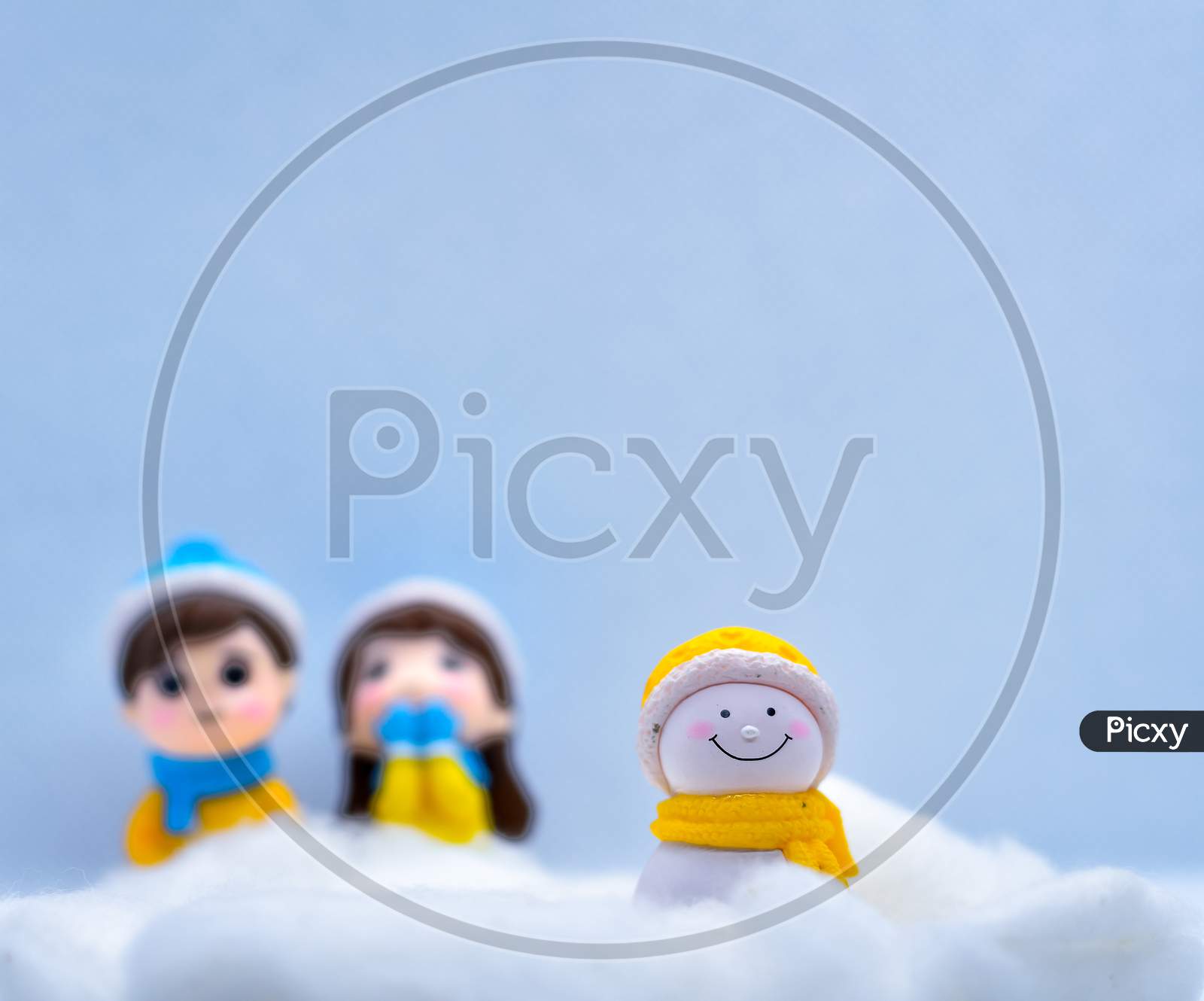 Tourism And Travel Concept: Miniature Little Snowman In Winter Snow With Couple In The Background