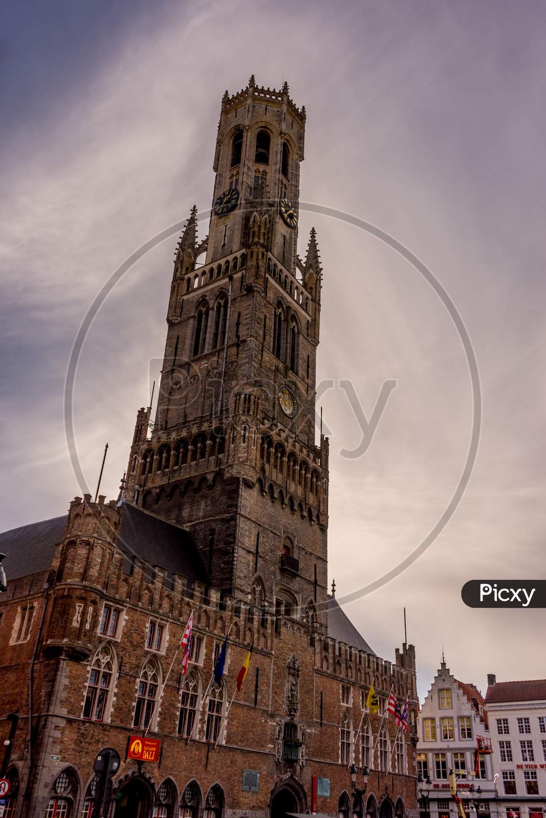 Bruges, Belgium - 17 February 2018: Belfry Of Bruges, A Group Of People Walking In Front Of A Clock Tower With Belfry Of Bruges In The Background