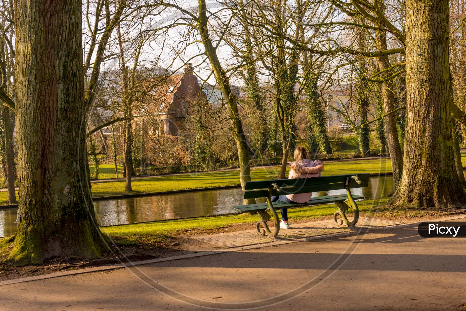Belgium, Bruges, Unknown Woman Sitting On A Bench By A Canal