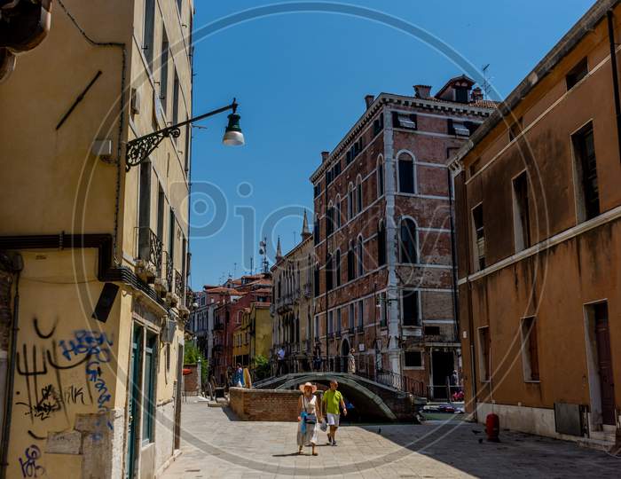 Venice, Italy - 01 July 2018: People Walking On Narrow Street Along Canal In Venice, Italy