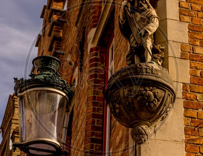 Belgium, Bruges, A Lamp Post In Front Of A Sculpture On A Wall