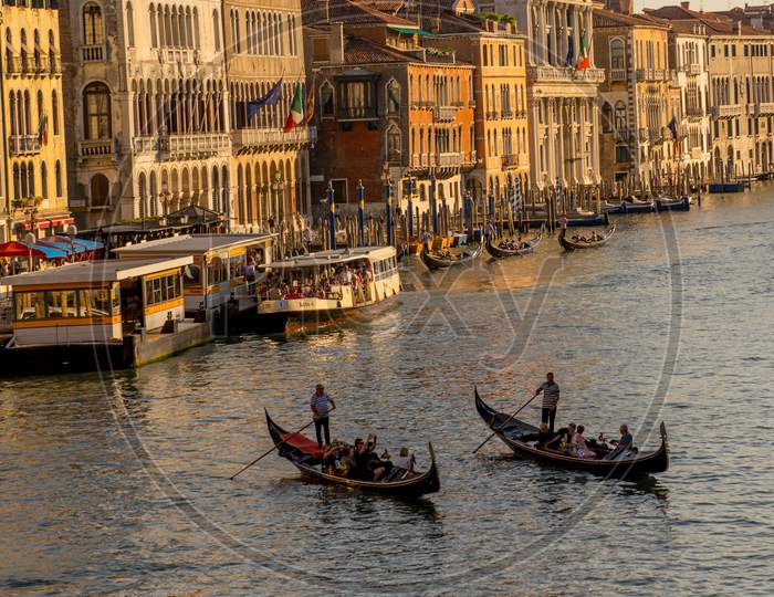 Gondolier Taking Tourists On A Gondola Ride Along The Grand Canal Near Rialto Hotel In Venice, Italy