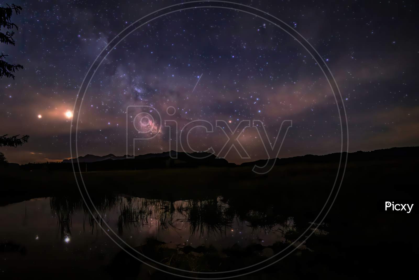 A starry night with thee Milky Way partly reflecting in a little pond at the so called Winklmoosalm in the Mountains of Reit im Winkl in Bavaria, Germany.