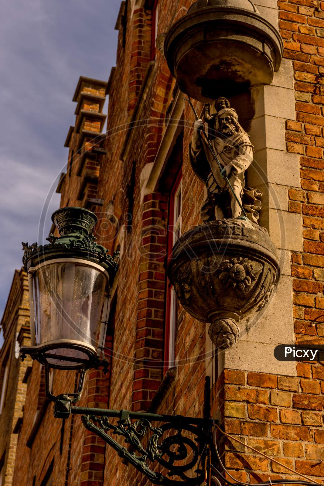 Belgium, Bruges, A Lamp Post In Front Of A Sculpture On A Wall