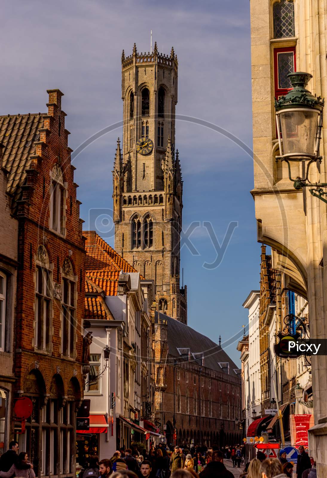 Bruges, Belgium - 17 February 2018: Belfry Of Bruges, A Group Of People Walking In Front Of A Clock Tower With Belfry Of Bruges In The Background