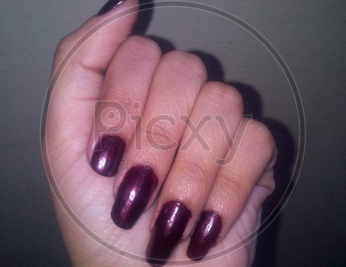 Wine color nail design. Red wine color manicure on girl hand. Shade of red on woman finger nails polish and grey background. Close up, selective focus