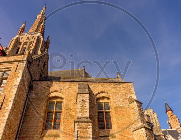 Belgium, Bruges, A Large Tall Tower With A Clock At The Top Of A Brick Building