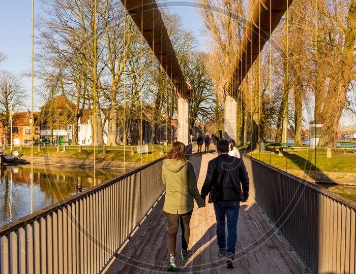 Belgium, Bruges,Unknown Couple Holding Hands And Walking On A Bridge