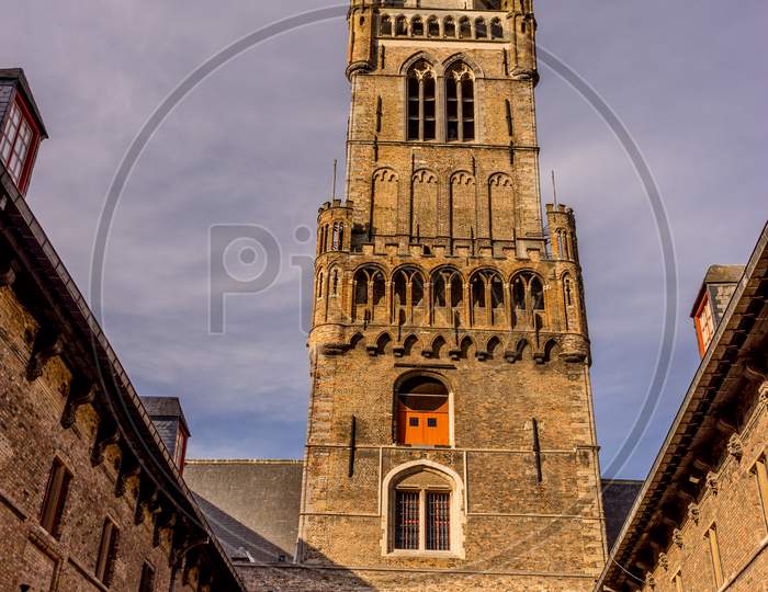 Belgium, Bruges, Belfry Of Bruges, A Large Brick Building With A Clock Tower With Belfry Of Bruges In The Background
